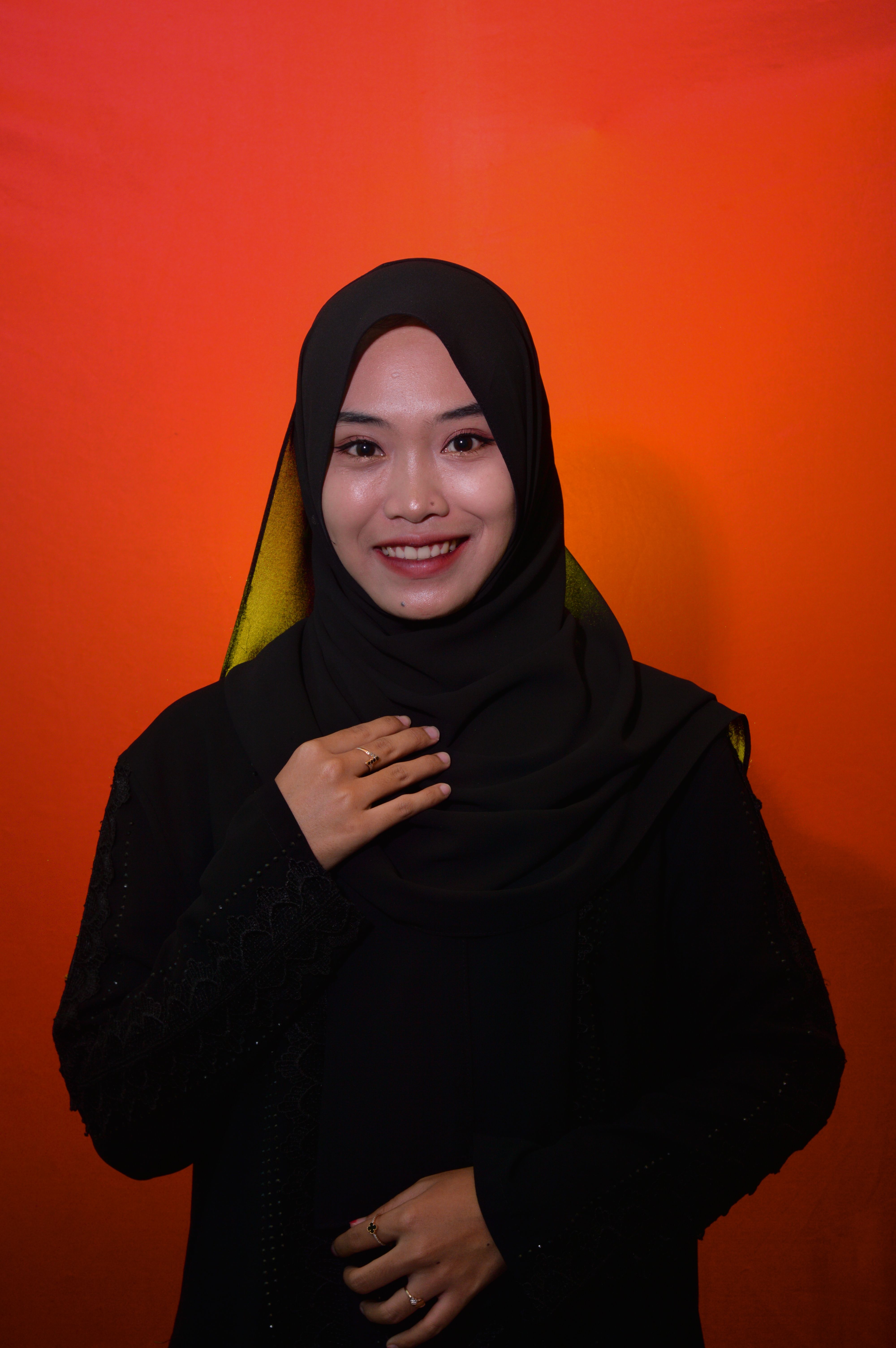 Portrait of a smiling woman wearing a black hijab against a red background, exuding warmth and confidence.