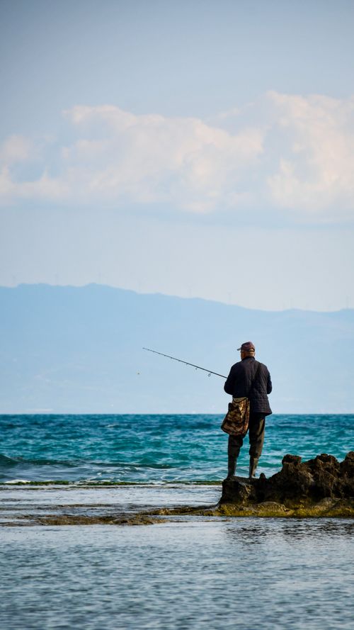 Free A man enjoys fishing on the rocky seashore of Yumurtalık, Adana, Türkiye, with stunning sea views. Stock Photo