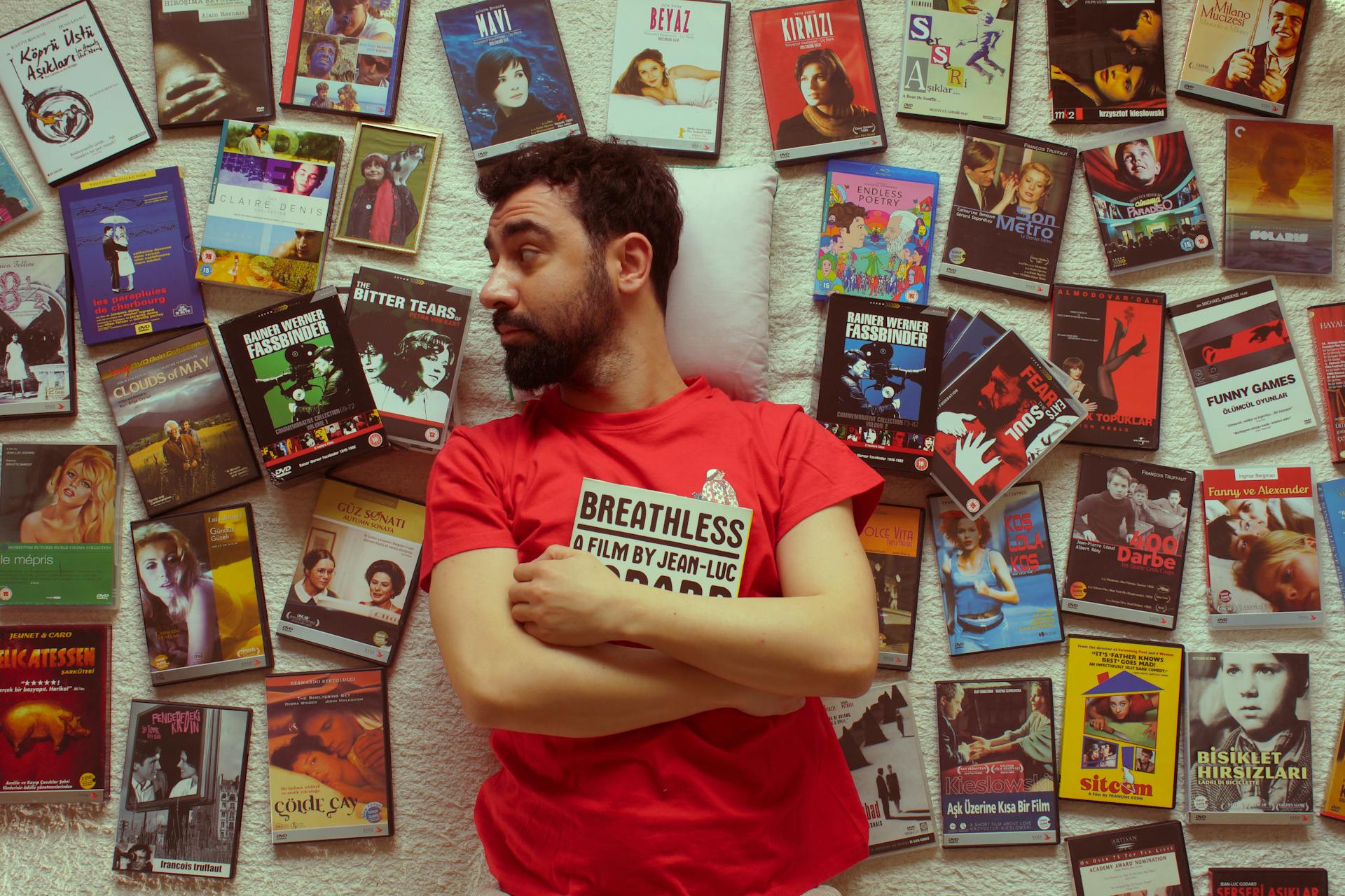 Man in Red T-Shirt Posing by DVD Movies Keep Cases on Wall