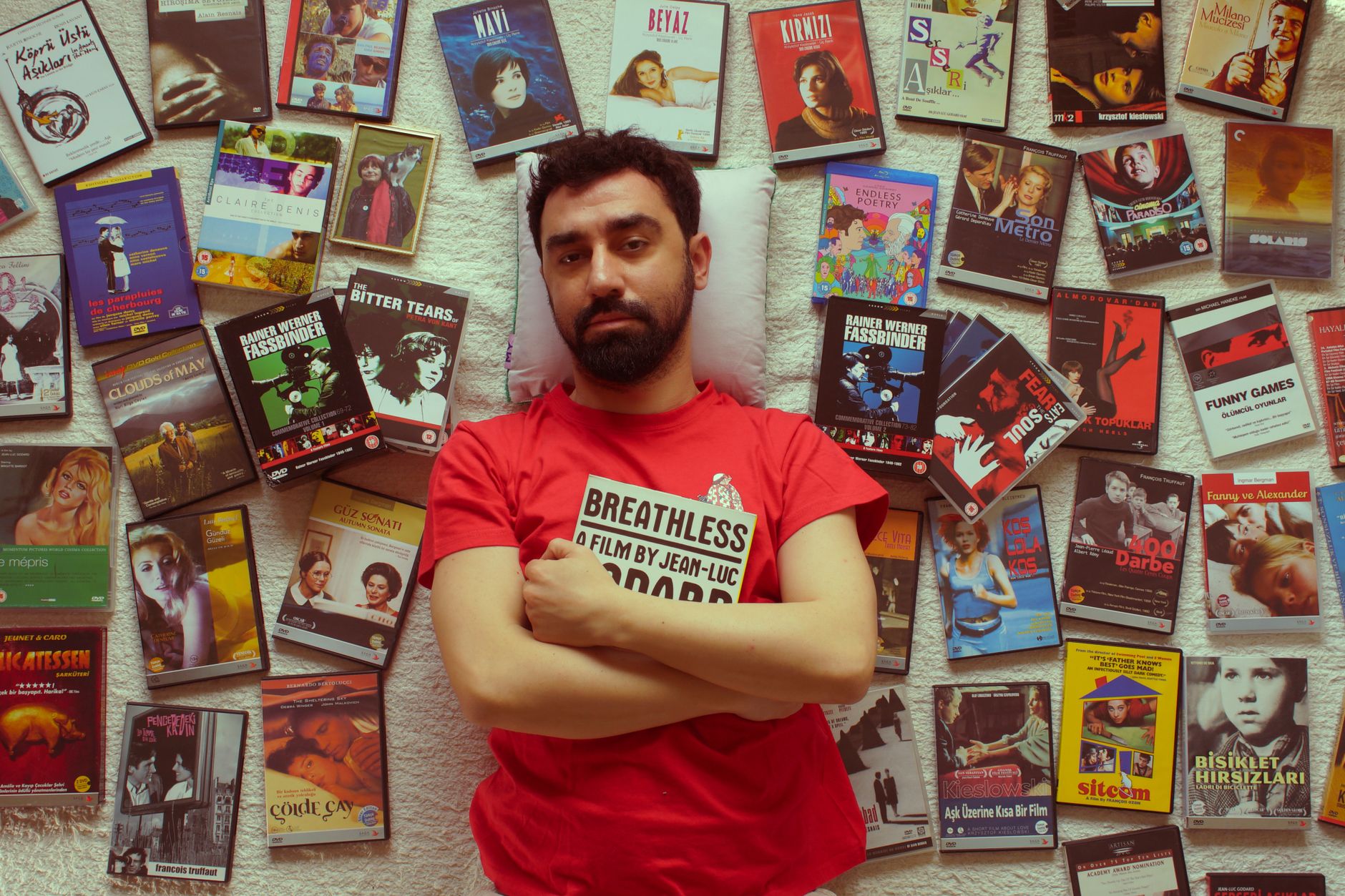 Uomo in maglietta rossa circondato da copertine di DVD, ideale per scegliere un film misterioso da vedere.