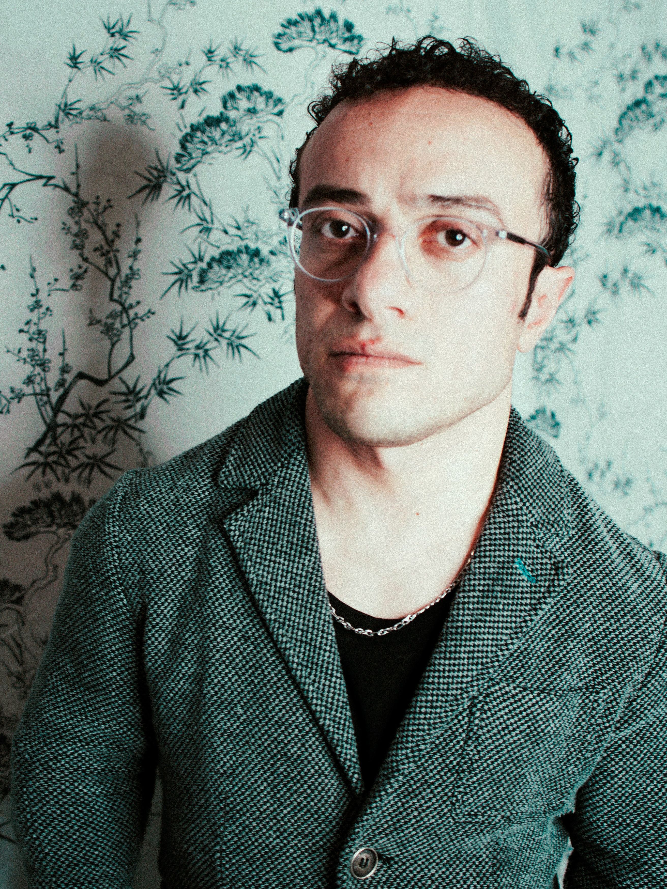 Portrait of a fashion-forward man in glasses and a patterned jacket.
