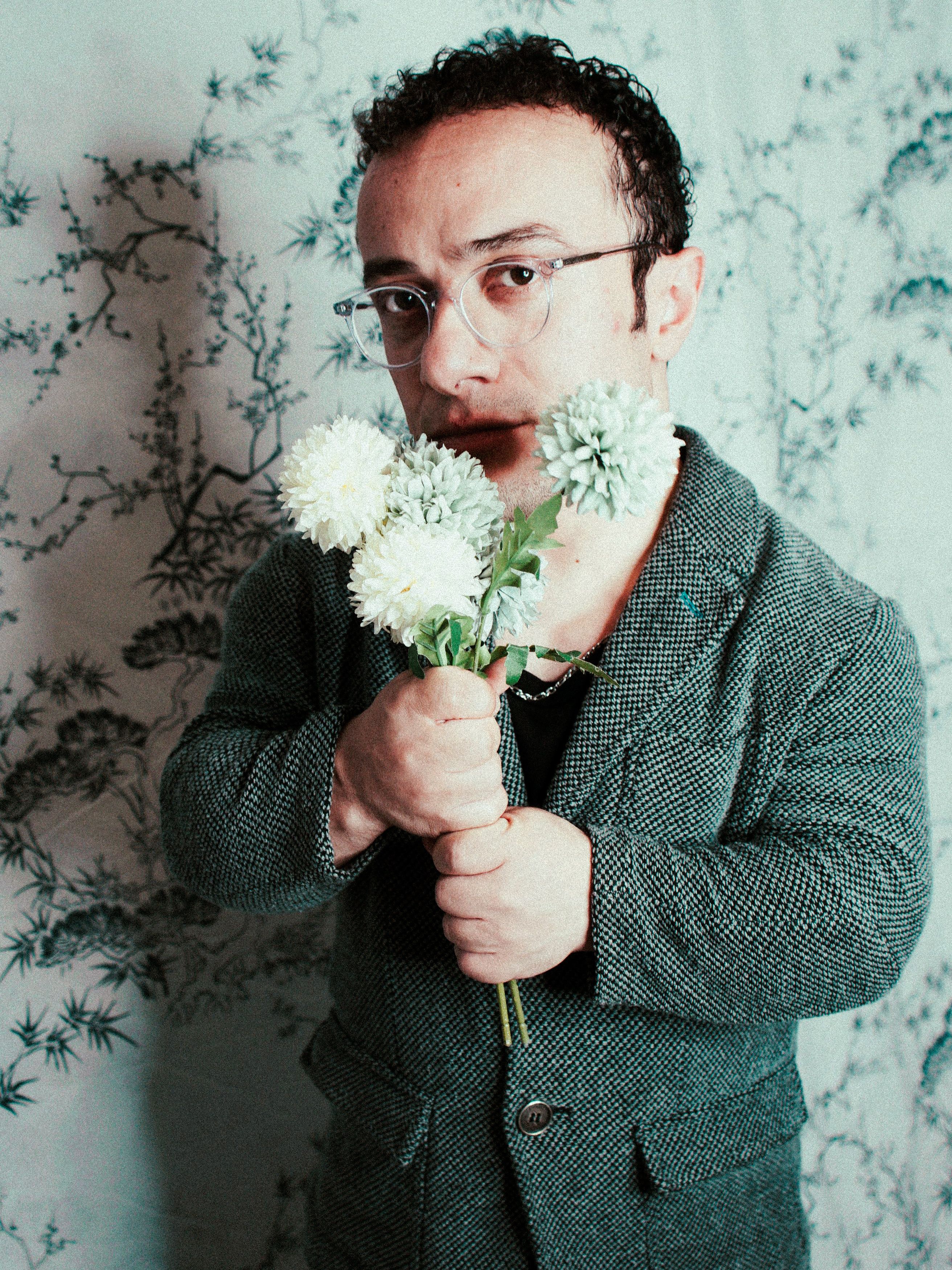 Portrait of a man in a suit holding a bouquet of white flowers indoors.