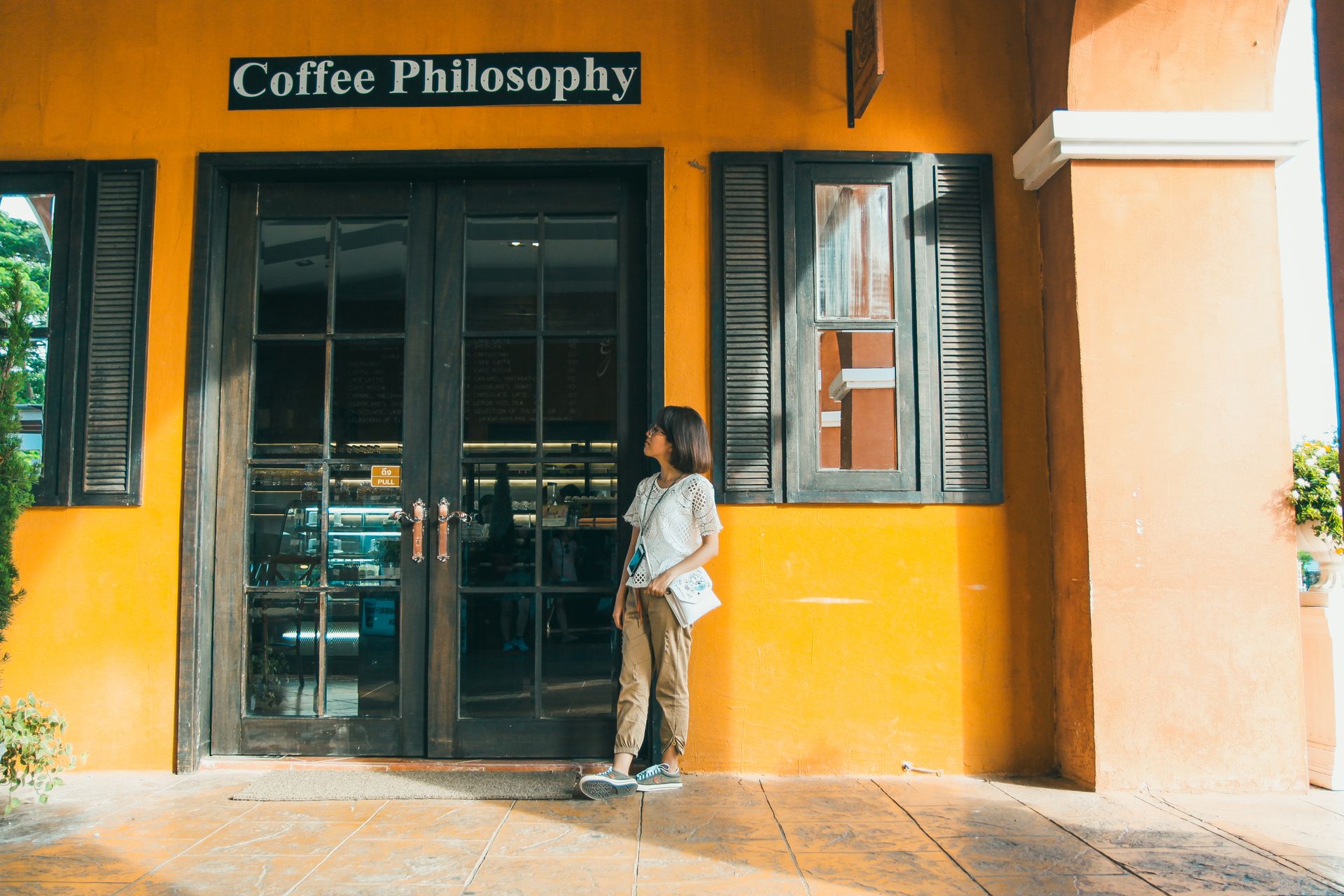 A woman stands outside a vibrant orange coffee shop with a welcoming glass door and sign.