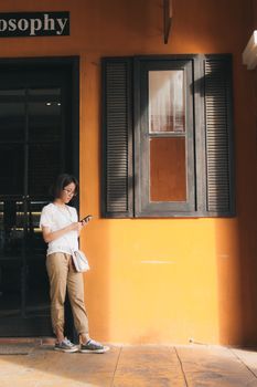 一名亚洲女性倚着橙色的门面发短信