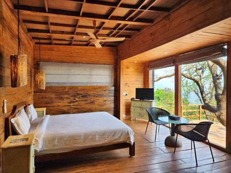 A cozy wooden bedroom interior with scenic forest views from Raigad, India.