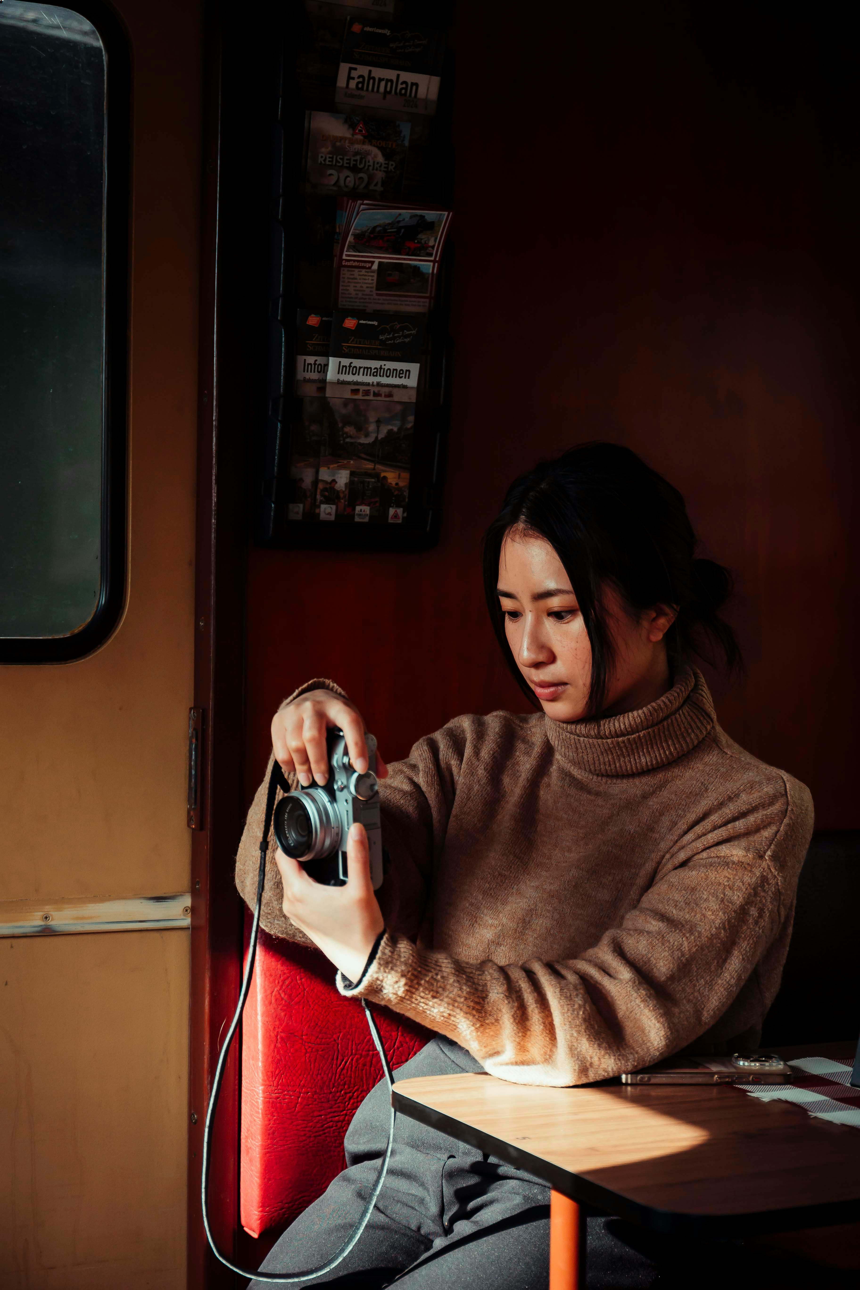 A young woman examines her camera in a cozy train compartment, capturing a serene travel moment.