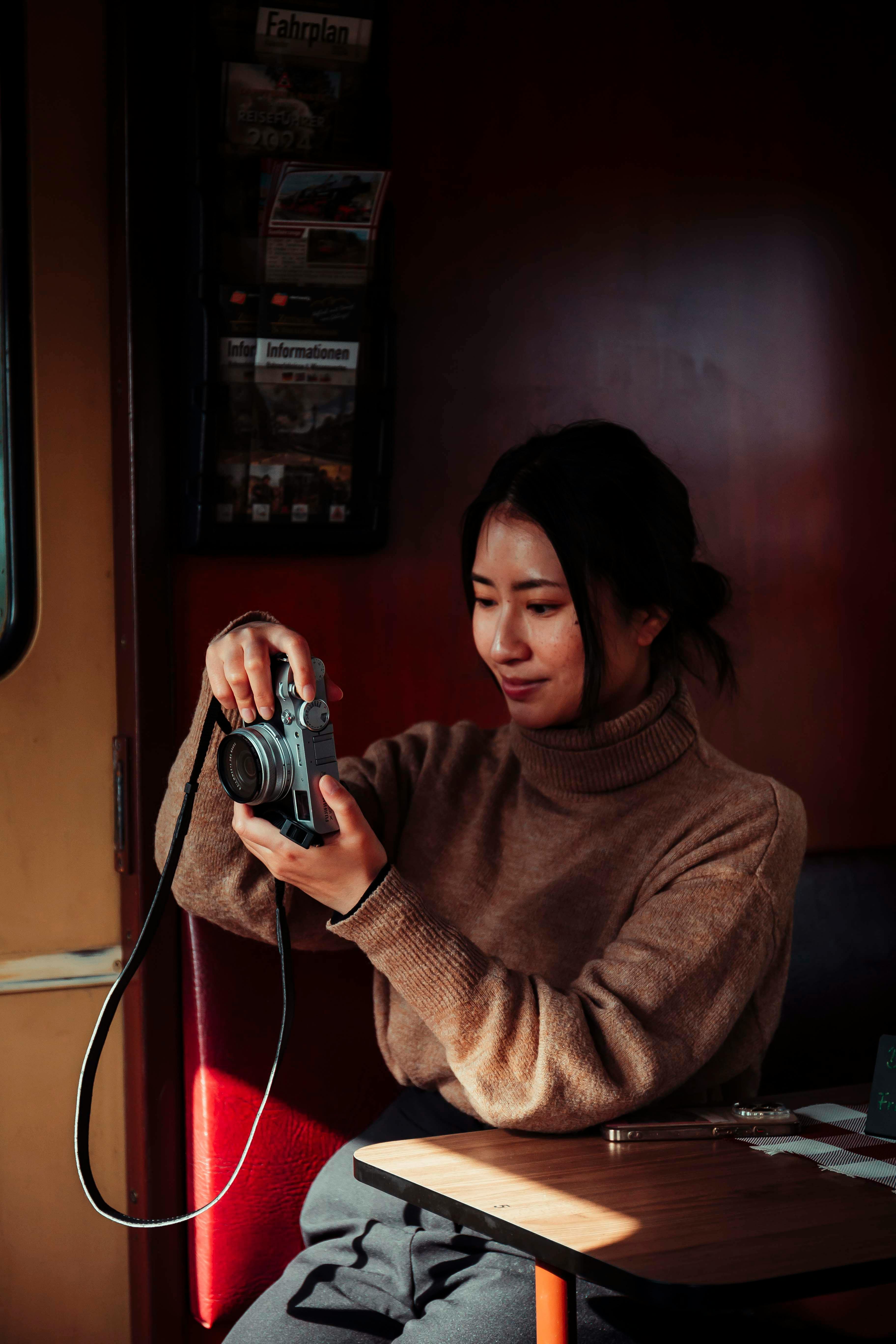 Young Asian woman enjoying photography inside, captured in warm tones.