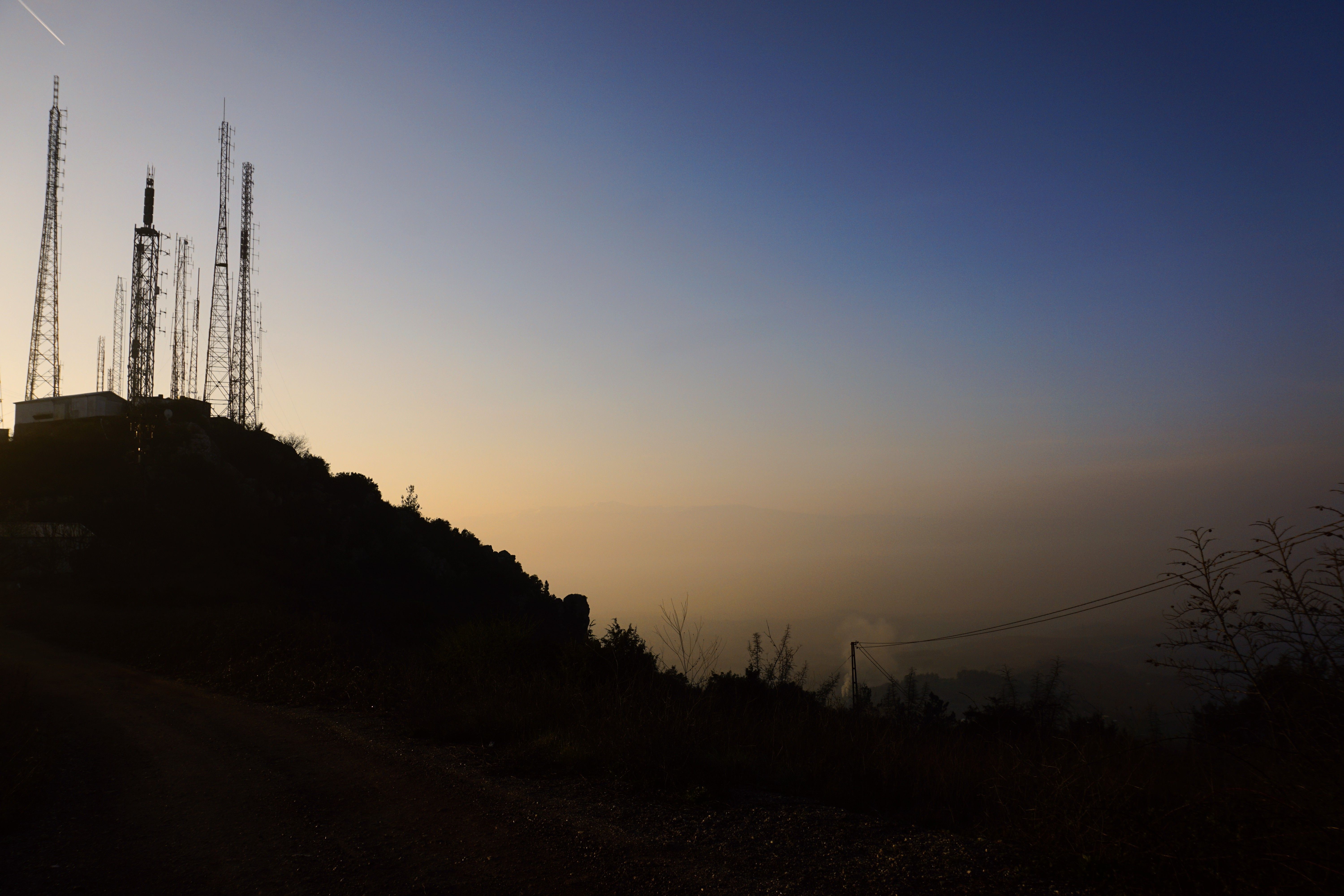 Silhouette of transmission towers on a hill during dawn with clear sky.