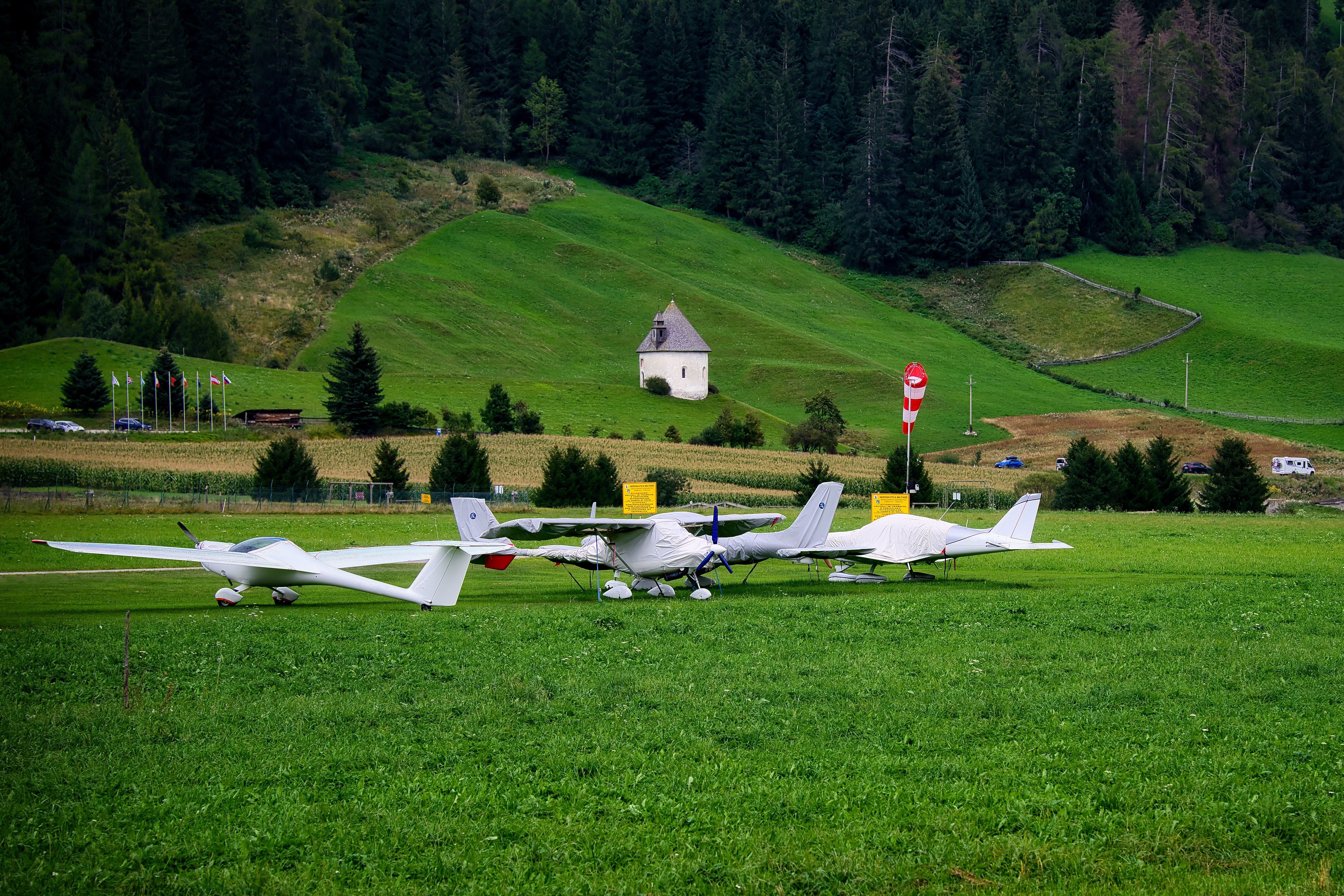 Small aircraft on a grass runway with green hills and a chapel in the background.