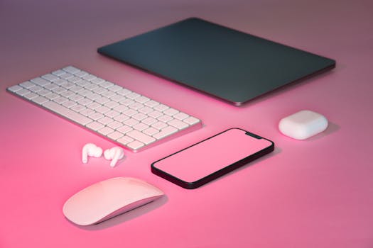 Stylish desk setup featuring a laptop, keyboard, mouse, and smartphone with pink accents.