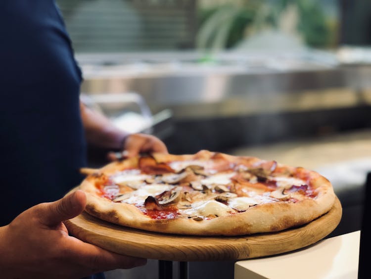 Person Holding Whole Pan Of Baked Pizza