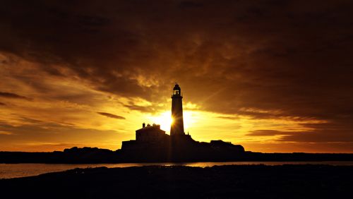 Free Stunning silhouette of St. Mary's Lighthouse against a vibrant sunset sky. Stock Photo