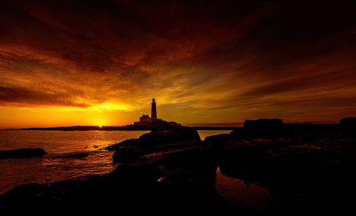 Free Beautiful sunset view of St Mary's Lighthouse with dramatic sky and rocky shore. Stock Photo