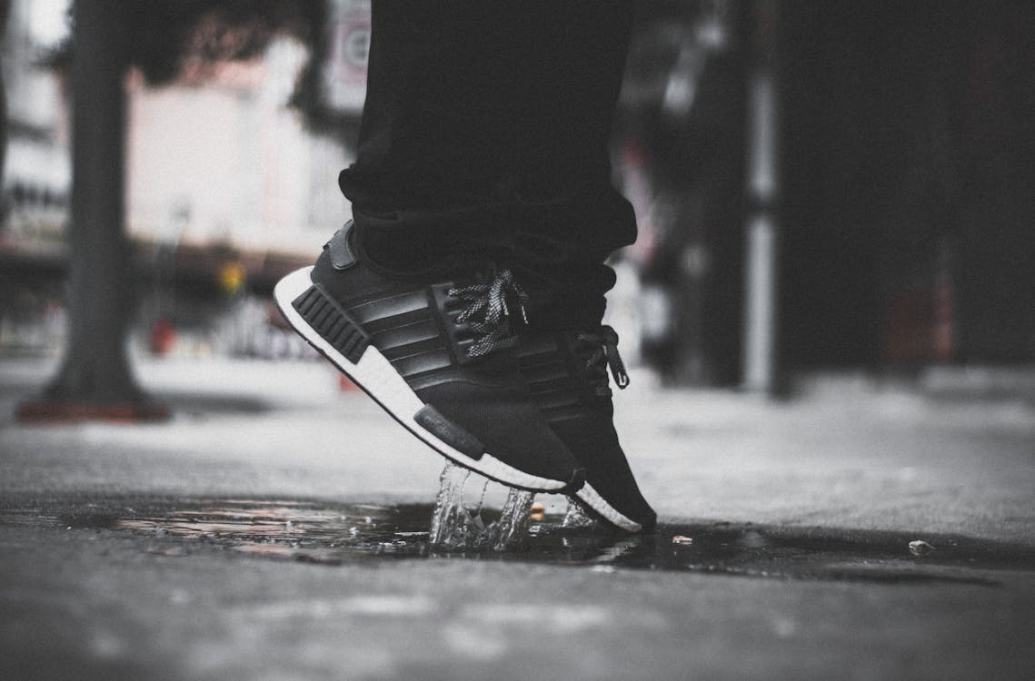 Free Grayscale Photo of Person Wearing Adidas Nmd Jumping on Puddle Stock Photo