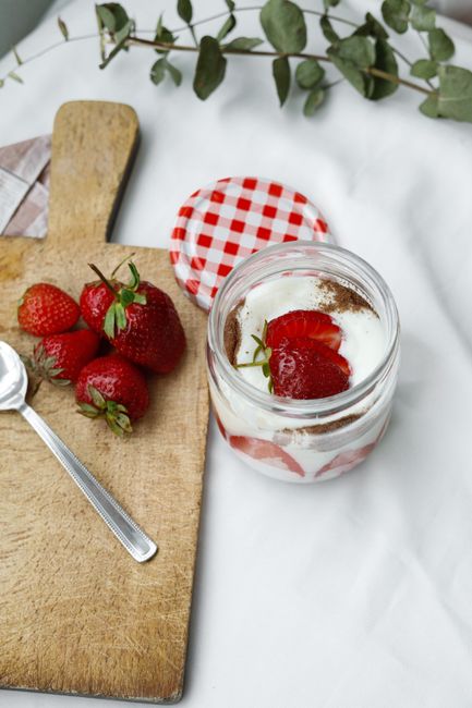 A glass jar of pink strawberry yogurt topped with sliced fresh strawberries and a drizzle of the fruit syrup running down the side.