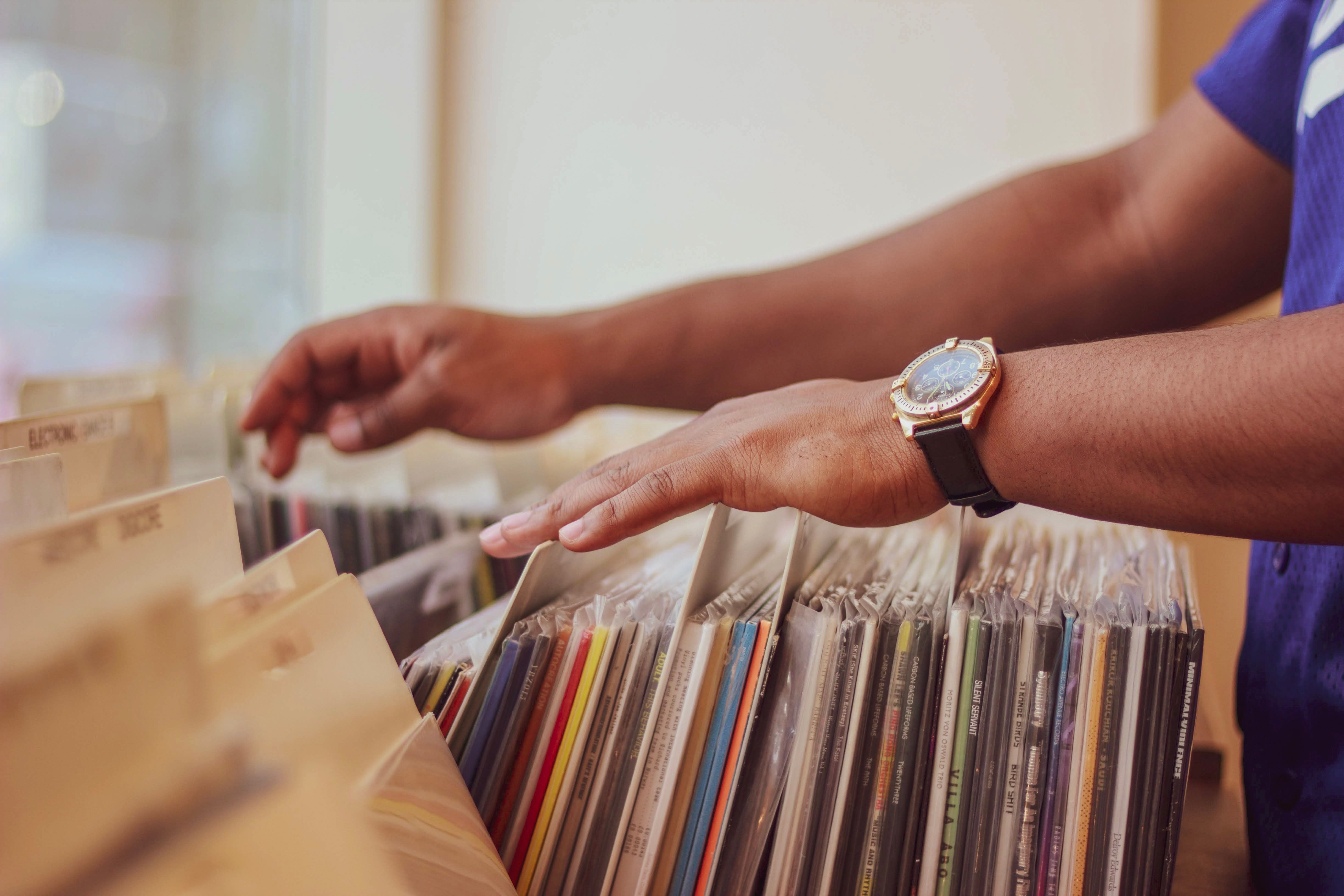 Mão folheando uma coleção de vinil com proximidade e intenção.