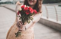 阳光明媚的日子里，一个穿着花裙子的女人，拿着一束充满活力的红玫瑰，面带微笑
