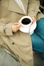 Close-up of Woman in Jeans and a Trench Sitting and Holding a Cup of Coffee
