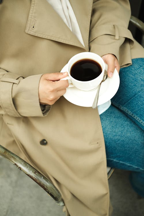 Free Close-up of Woman in Jeans and a Trench Sitting and Holding a Cup of Coffee Stock Photo