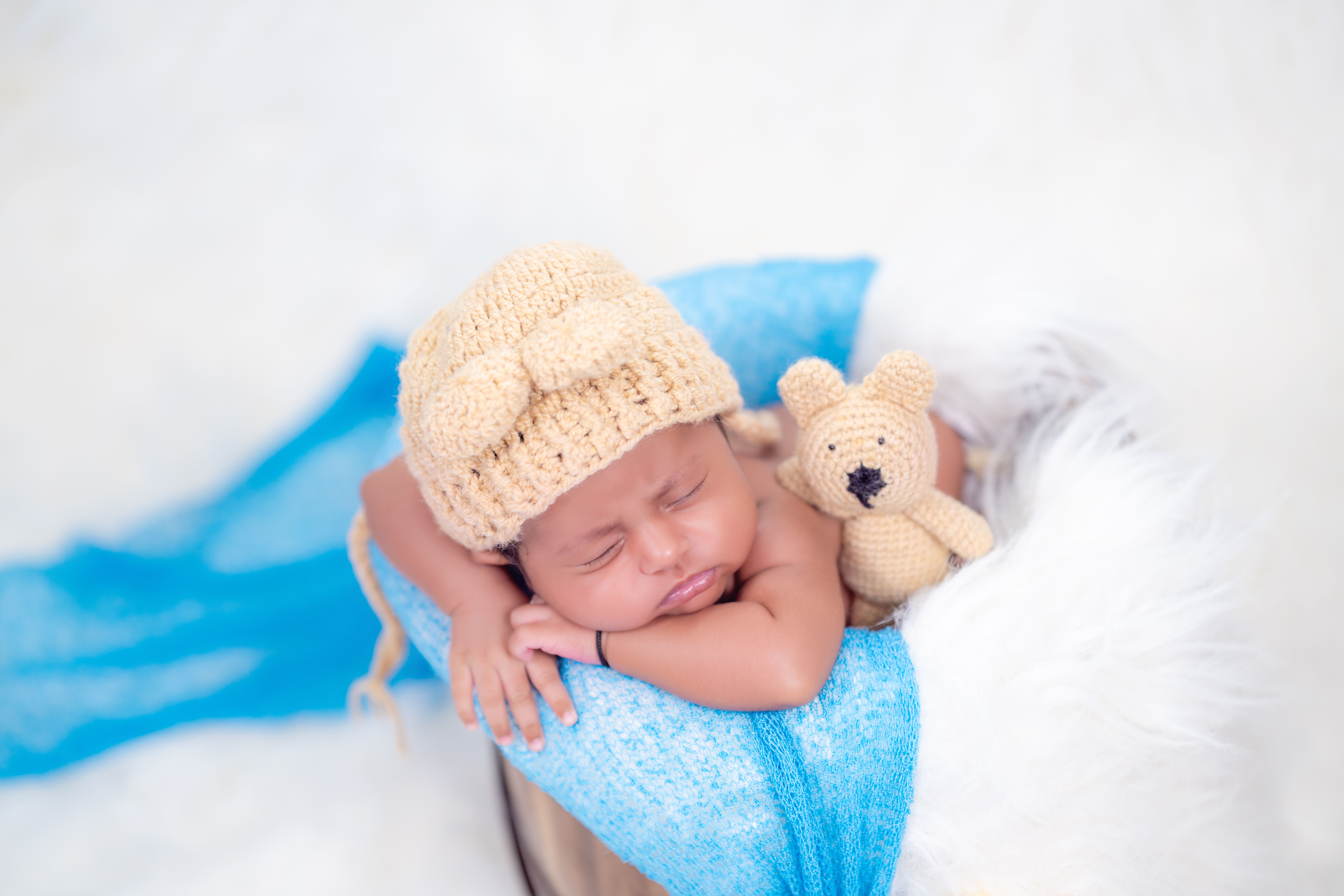 Adorable newborn baby sleeping peacefully with a teddy bear, wearing a knit hat in a cozy setup.