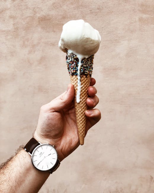 Hand holds a melting vanilla ice cream cone with sprinkles, showcasing a casual lifestyle moment.