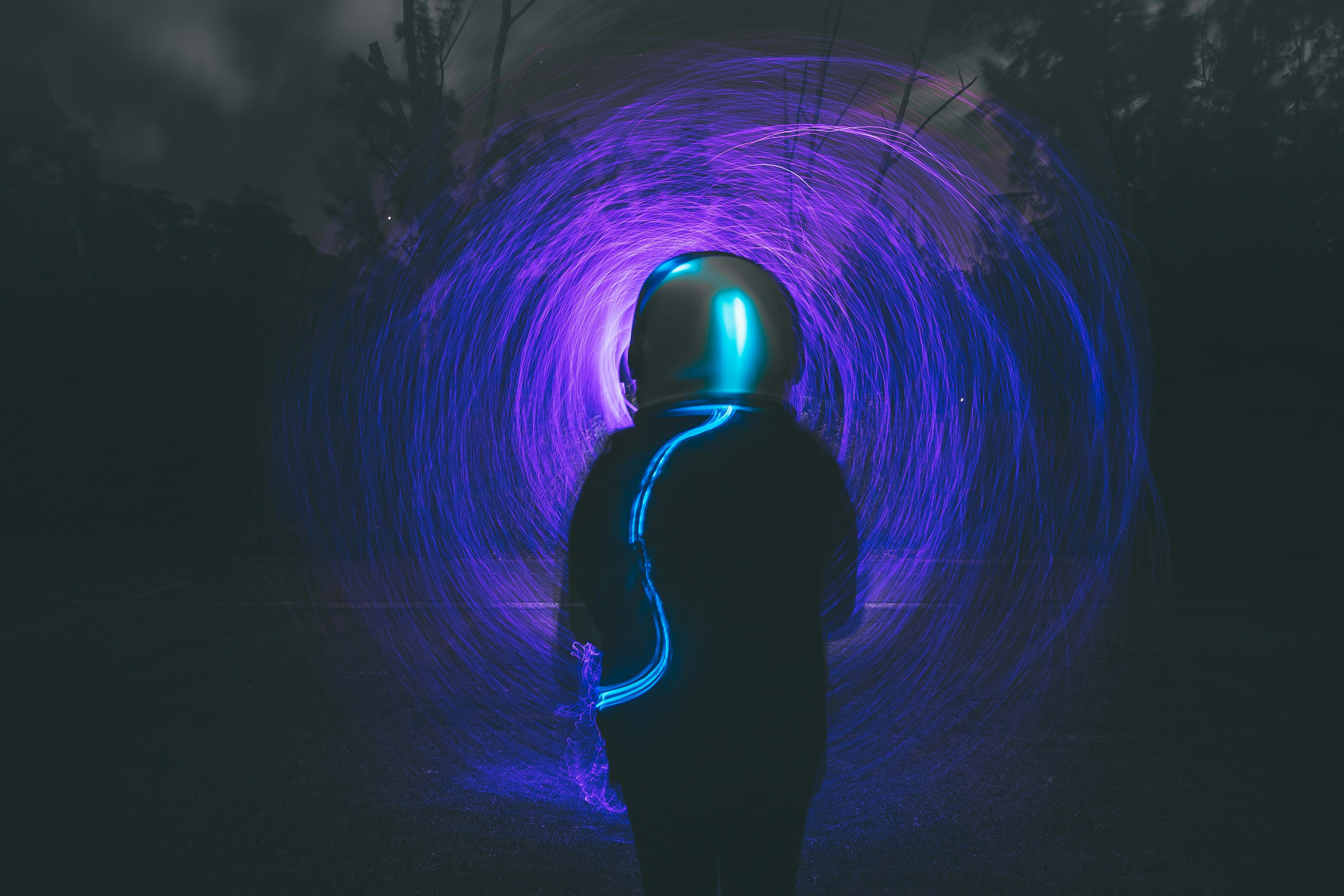 Astronaut silhouette with vibrant blue and purple light trails in a night forest setting.