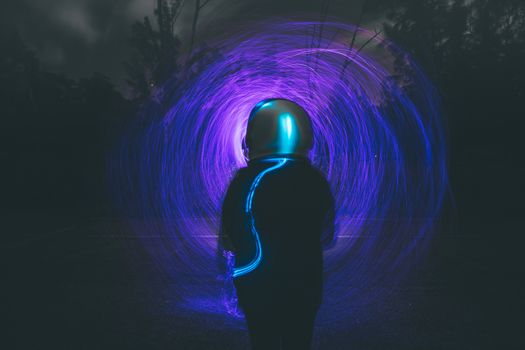 Astronaut silhouette with vibrant blue and purple light trails in a night forest setting.