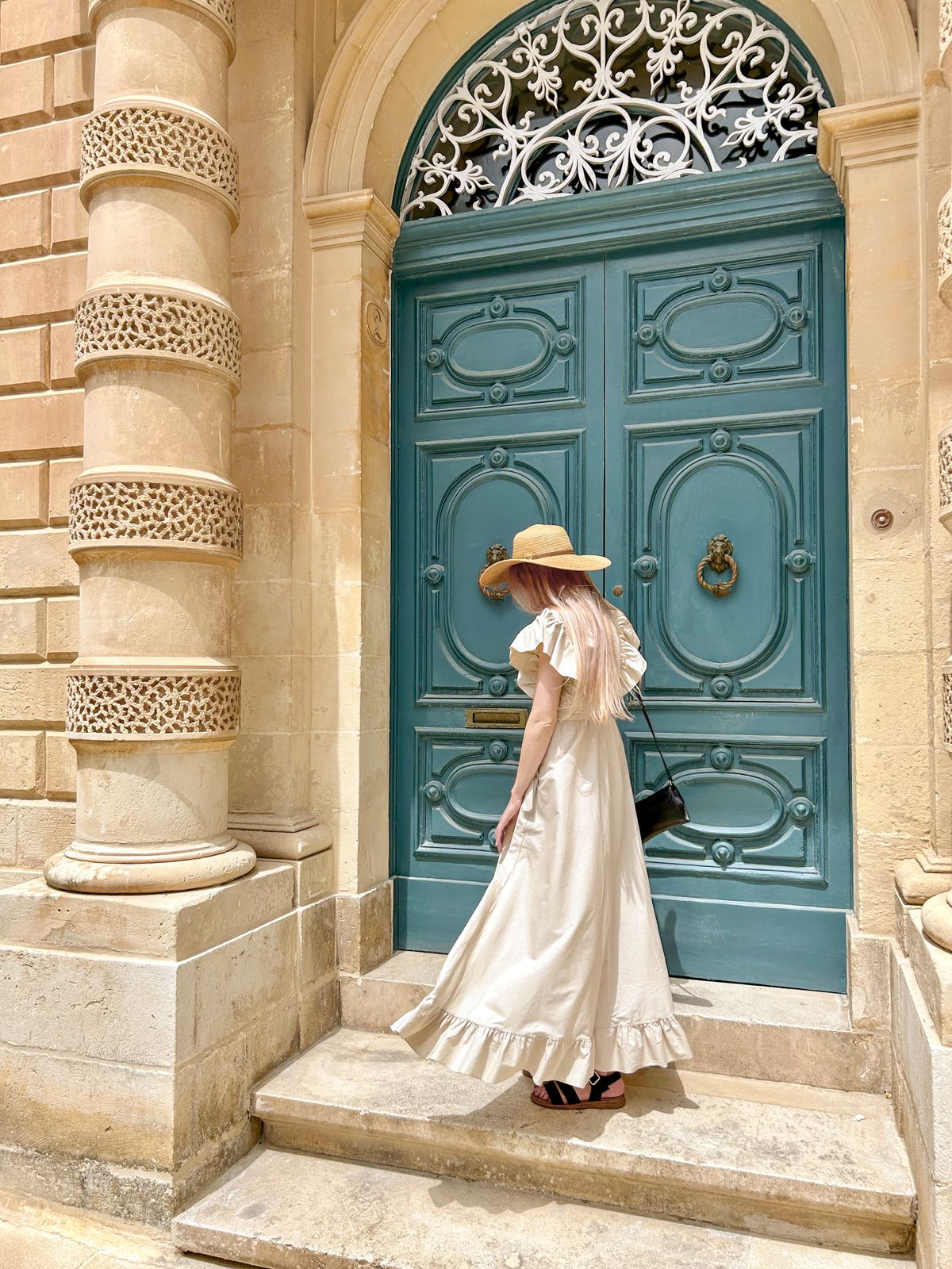 Woman in a hat and white dress standing near a column and door