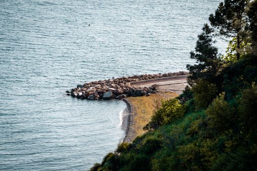 Free Serene coastal landscape featuring lush green hills and a tranquil sea shore under natural light. Stock Photo