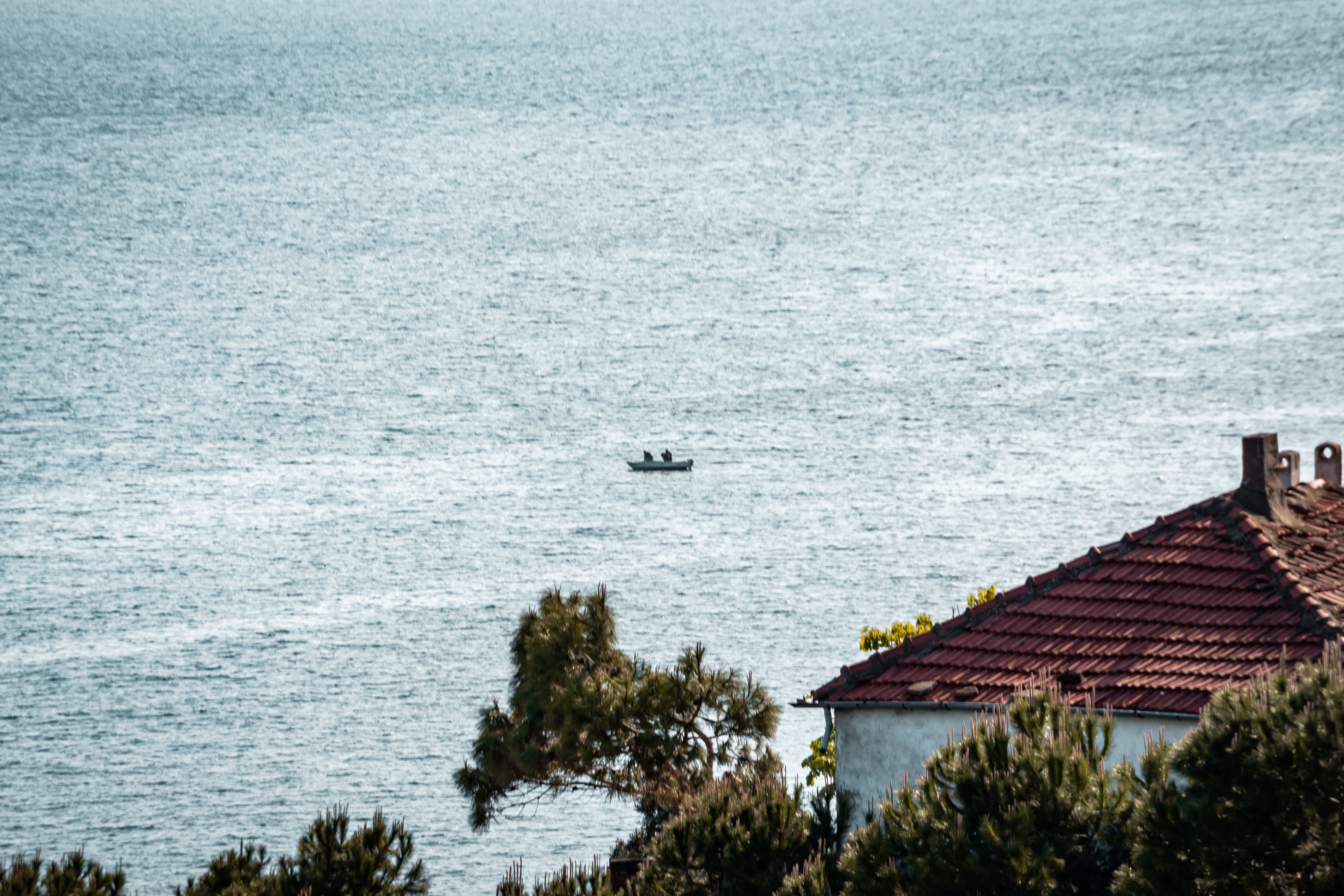 A tranquil seaside scene featuring a lone motorboat on the water and tiled rooftops in the foreground.