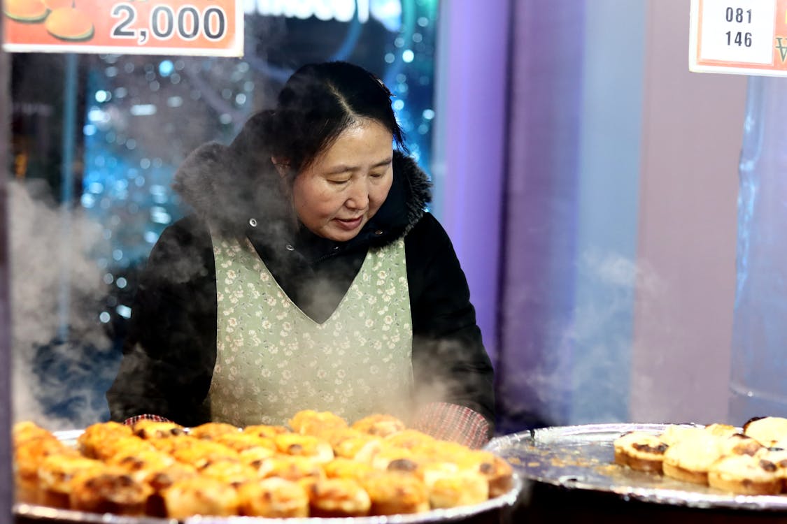 Free An Asian woman cooking steaming street food on a winter night with a festive atmosphere. Stock Photo