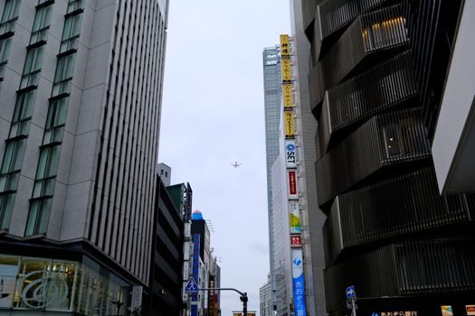 A dynamic urban view in Shibuya, Tokyo with tall buildings and an airplane overhead.