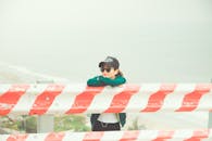 雾气弥漫的海边，一个女人戴着太阳镜和帽子，靠在红白相间的屏障上