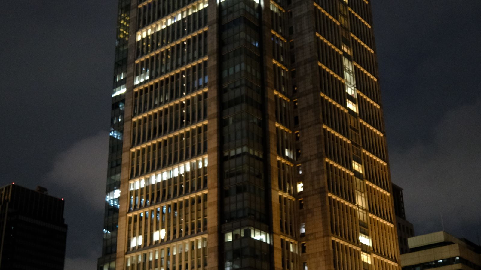 夜の丸の内ビル群がライトアップされ、金融街の力強さと不確実性を象徴する都市景観のイメージ