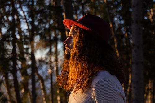 Free A portrait of a man in a red hat illuminated by sunlight against a backdrop of forest trees. Stock Photo