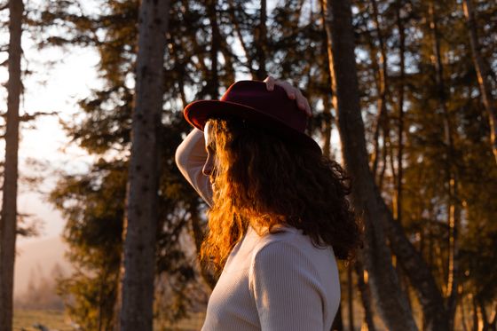 Woman in a hat standing in a sunlit forest, photo by Andrea Belmondo on Pexels