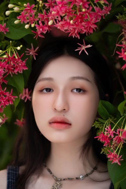 Close-up portrait of an Asian woman framed by vibrant pink flowers, exuding natural beauty.
