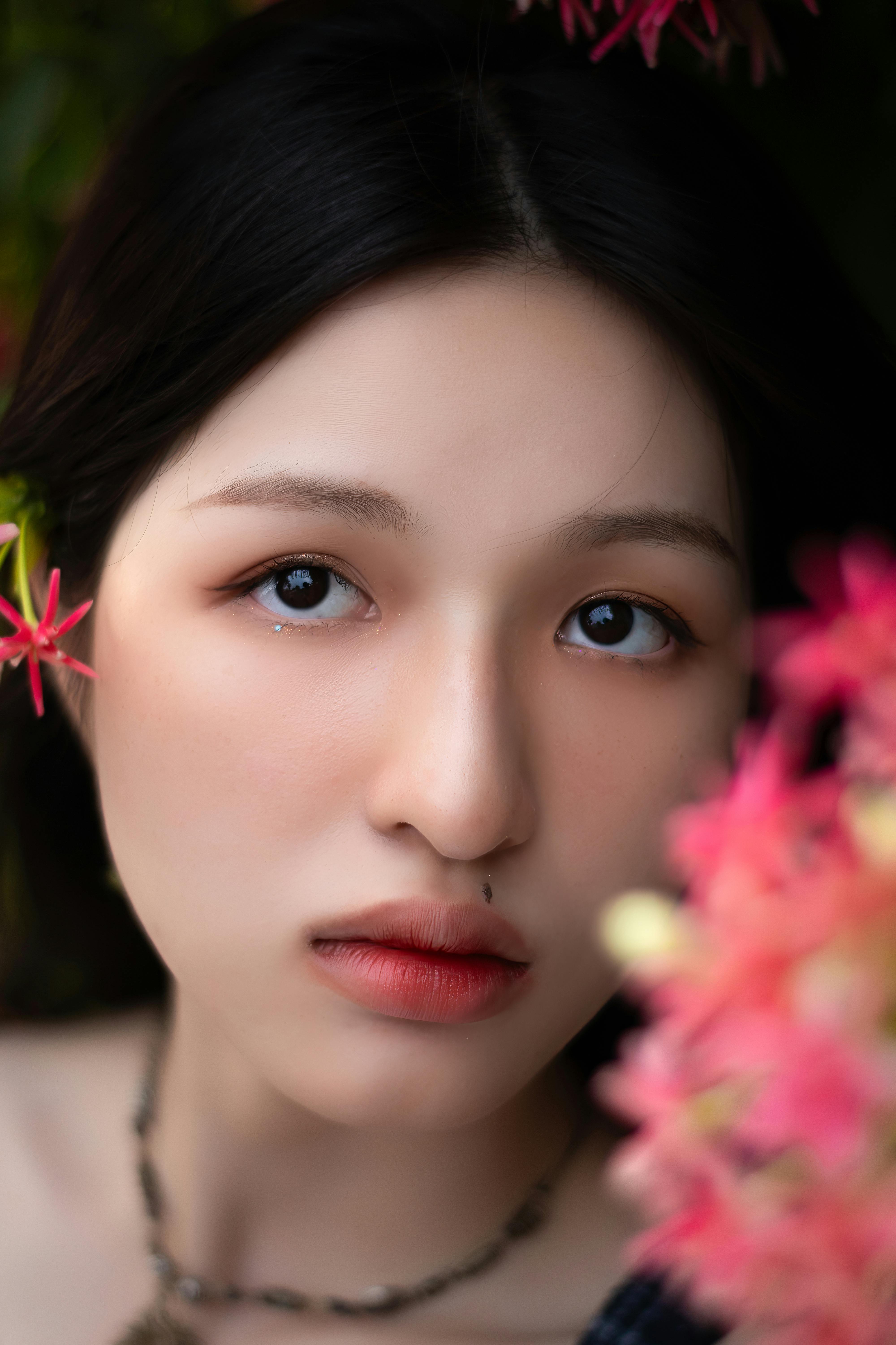 Intimate close-up portrait of a woman with black hair surrounded by pink flowers.