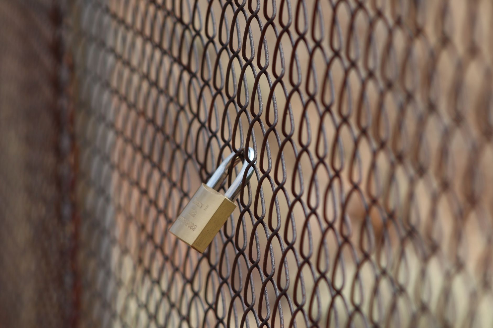 A closeup image of a metal padlock on a chain-link fence, symbolizing security and protection.