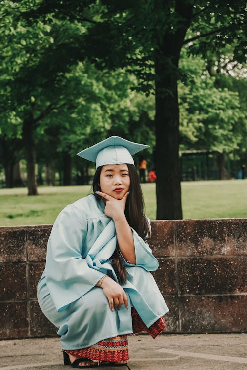 Femme Accroupie Portant Une Robe Académique Bleue Et Un Chapeau