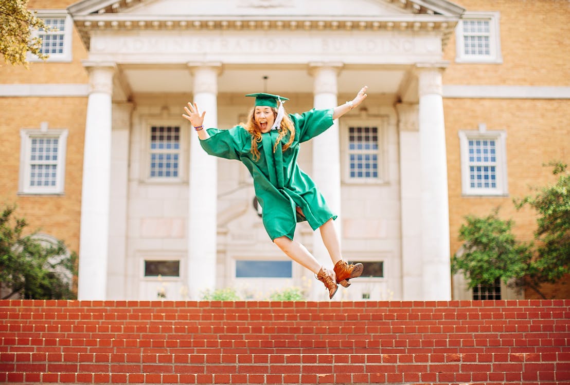 Woman jumping above stairs wearing graduation gown and a hat