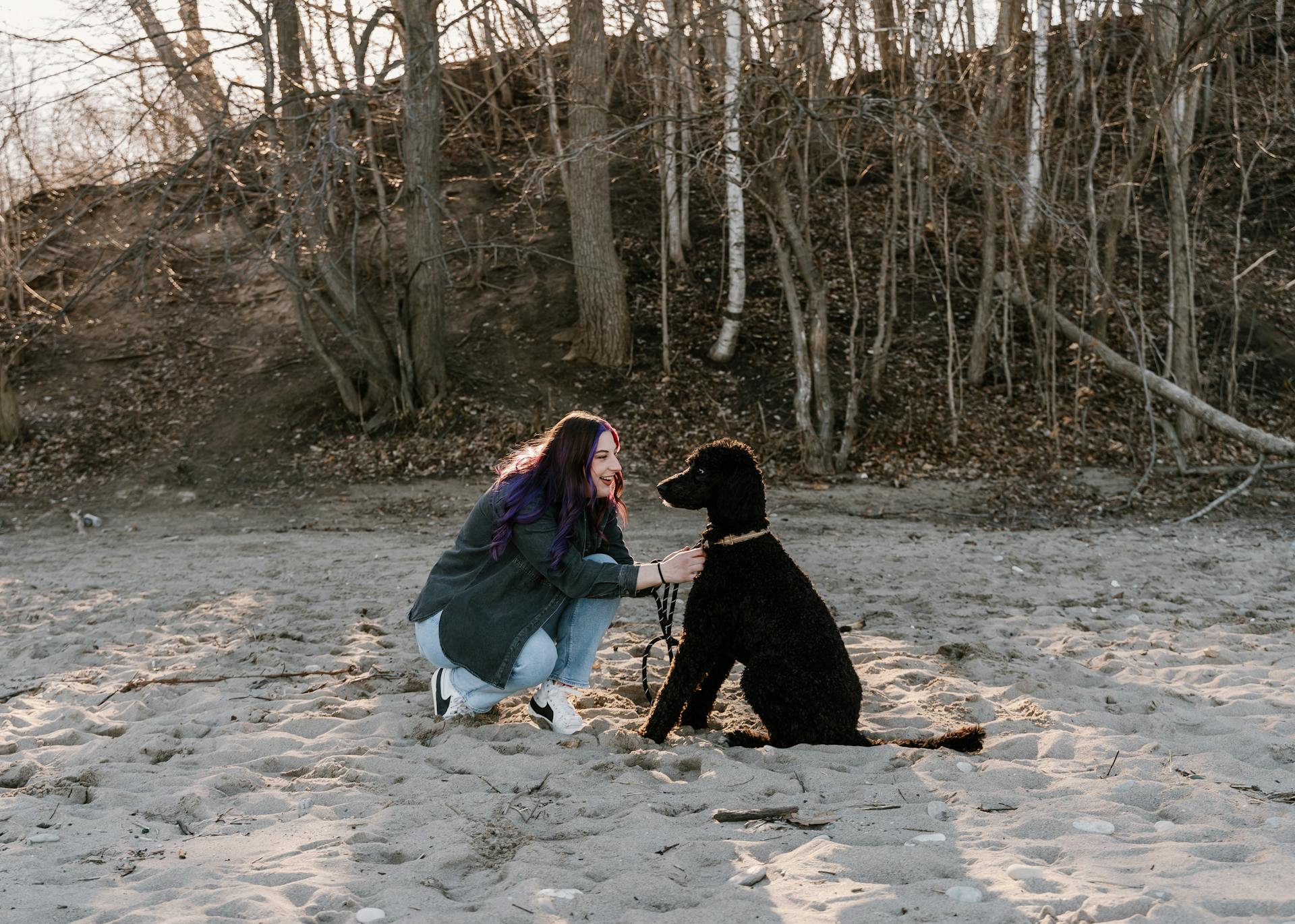 Une jeune femme accroupie sur une plage avec son caniche noir