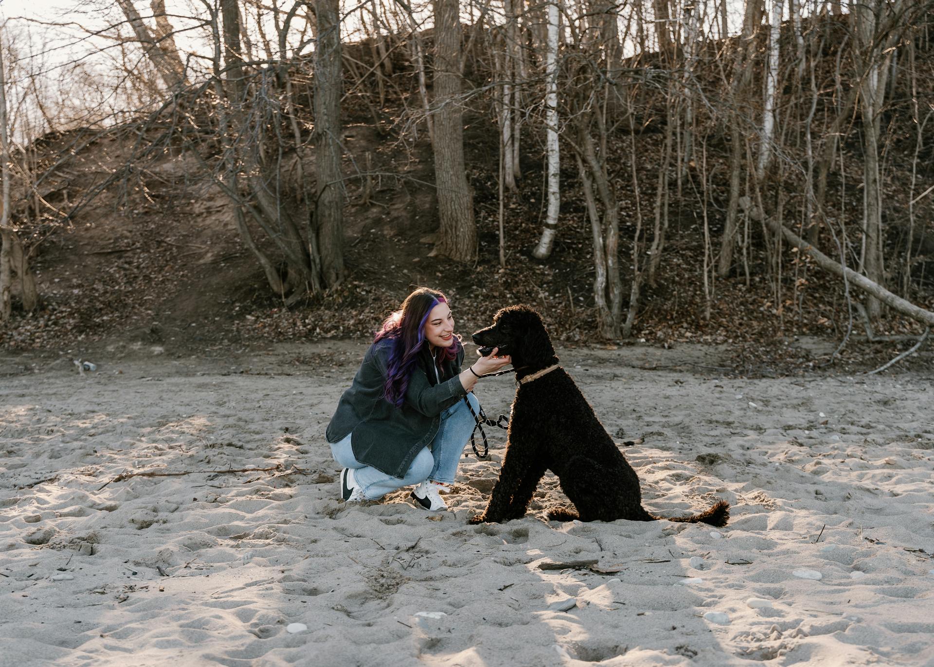 Une jeune femme accroupie sur une plage avec son caniche noir