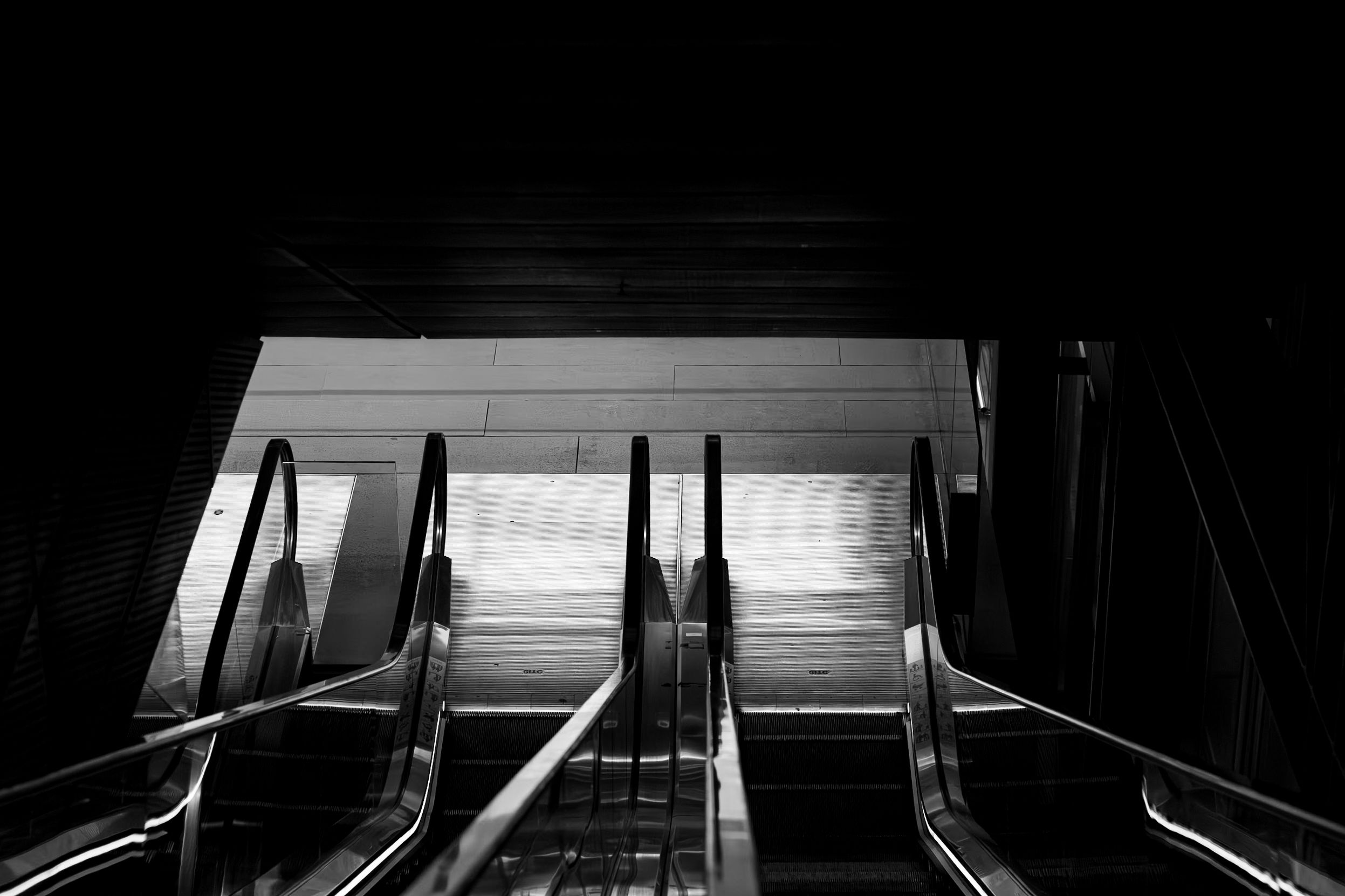 High-contrast black and white shot of subway station escalators from above.