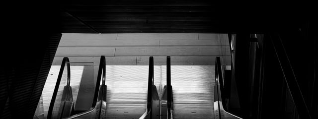 High-contrast black and white shot of subway station escalators from above.