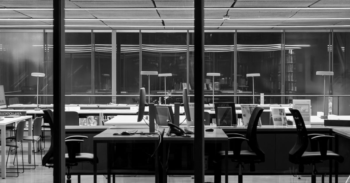 Foto elegante en blanco y negro de un moderno espacio de oficina vacío, con mobiliario elegante y grandes ventanales.