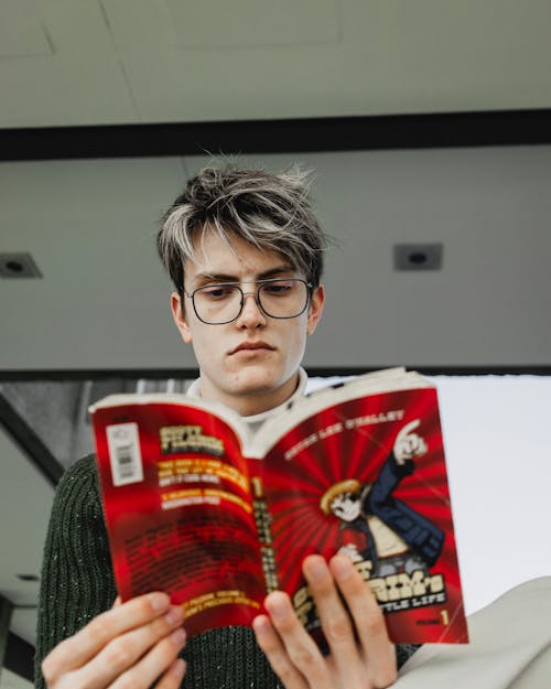 A young man with glasses reading a comic book
