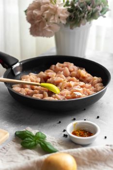 Raw chicken breast pieces in a frying pan with spices and herbs, ready for cooking.
