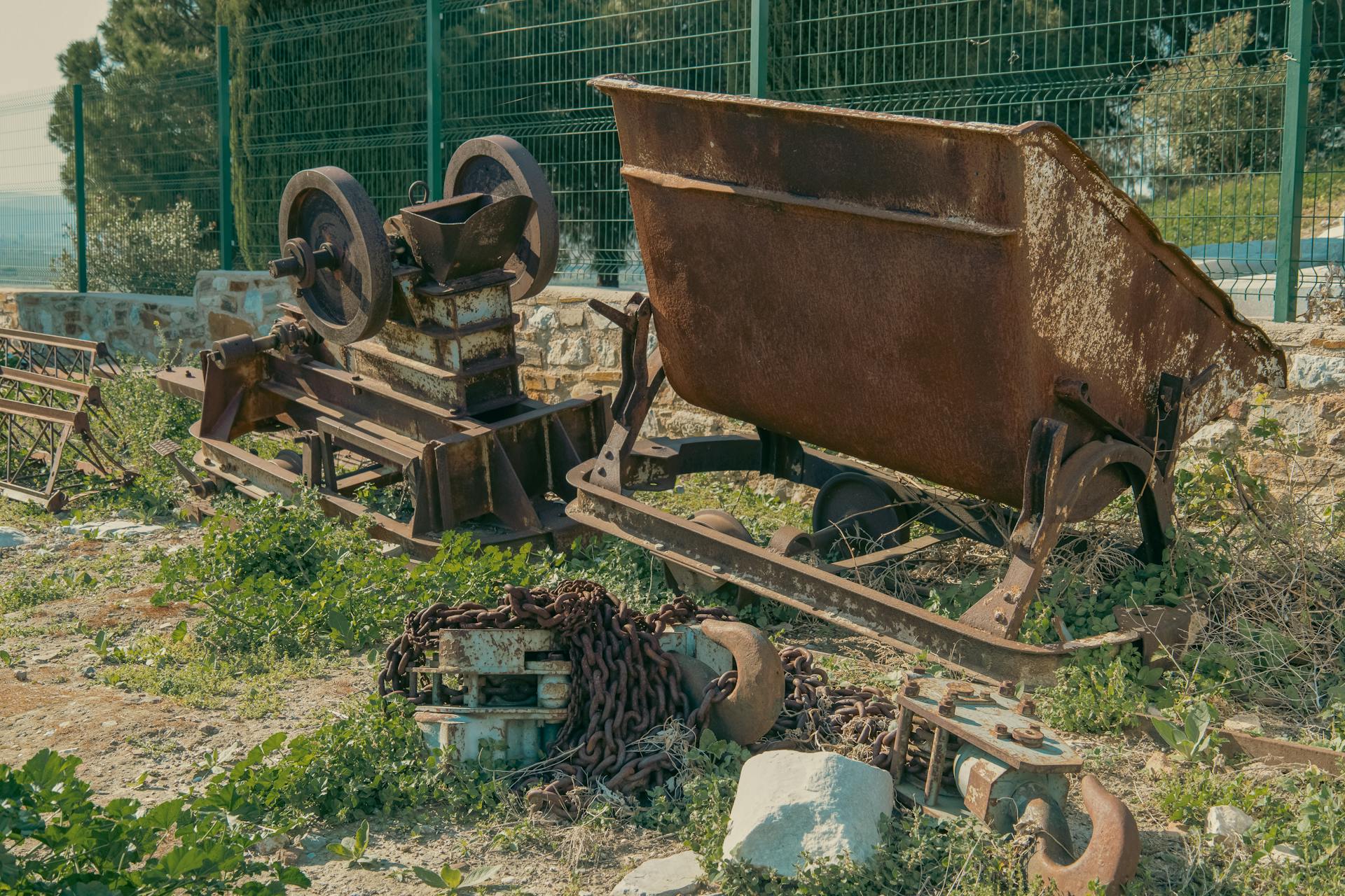 Rusty industrial machinery and scrap metal in an outdoor setting with greenery.