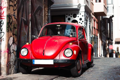 Free A striking red vintage car parked on a cobblestone city street lined with graffiti and urban buildings. Stock Photo